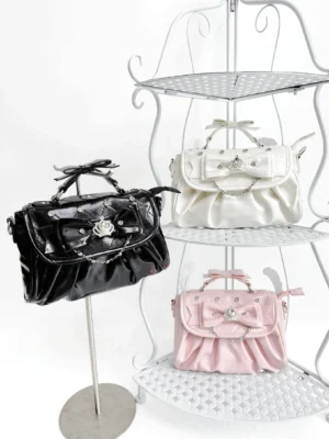 Three color variants of Jirai Kei crossbody bags with rhinestone crown bows displayed on metal tiered shelf showing pink white and black options