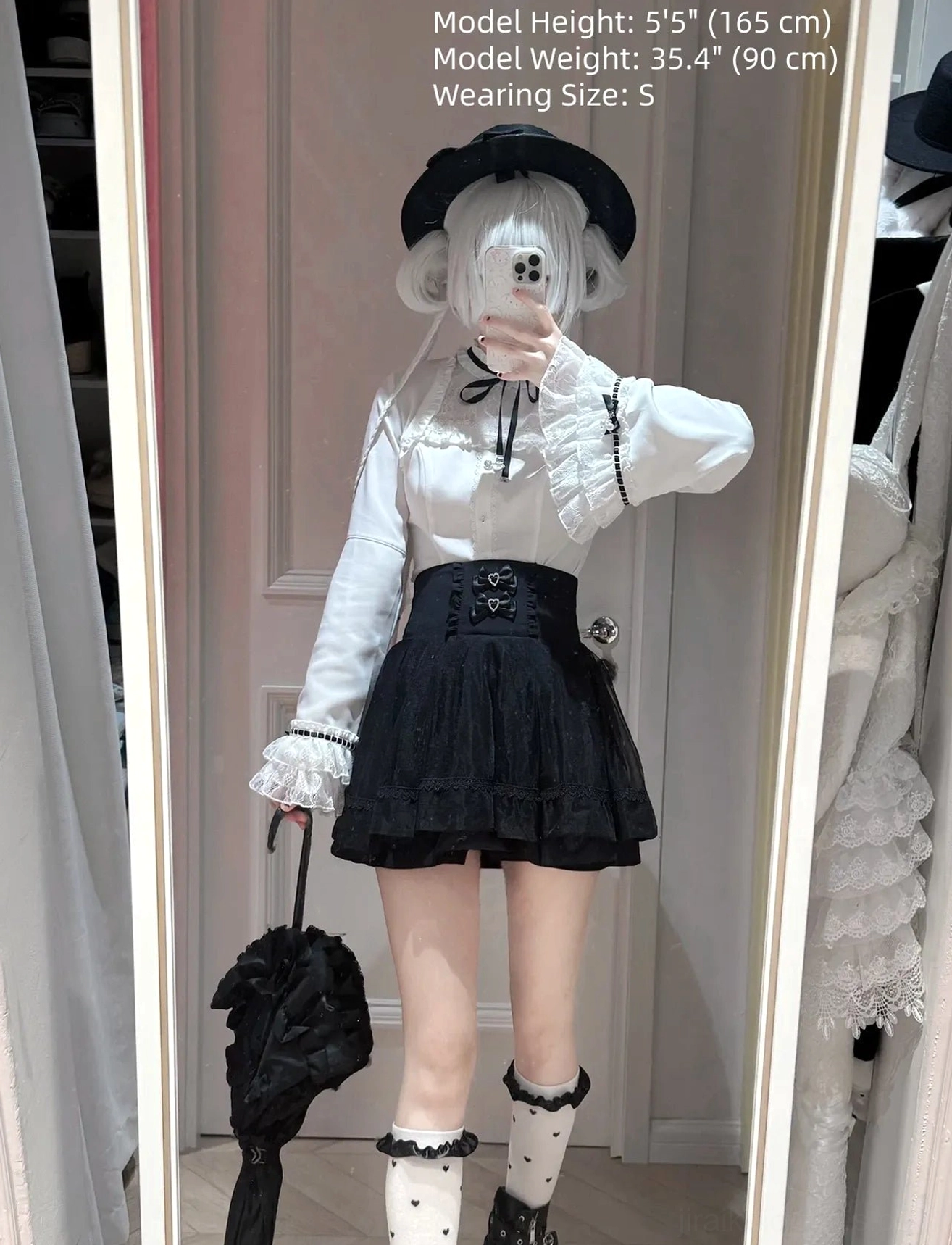 Full-body front mirror styling of jirai kei blouse and high-waist a-line skirt with double heart buckles, paired with black bowler hat, lace socks, and black parasol