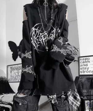 Black and white Jirai Kei cold-shoulder sweatshirt with gothic typography print, front upper-body view on punk female model in gothic interior space, white oversized lettering, stud-trimmed edges