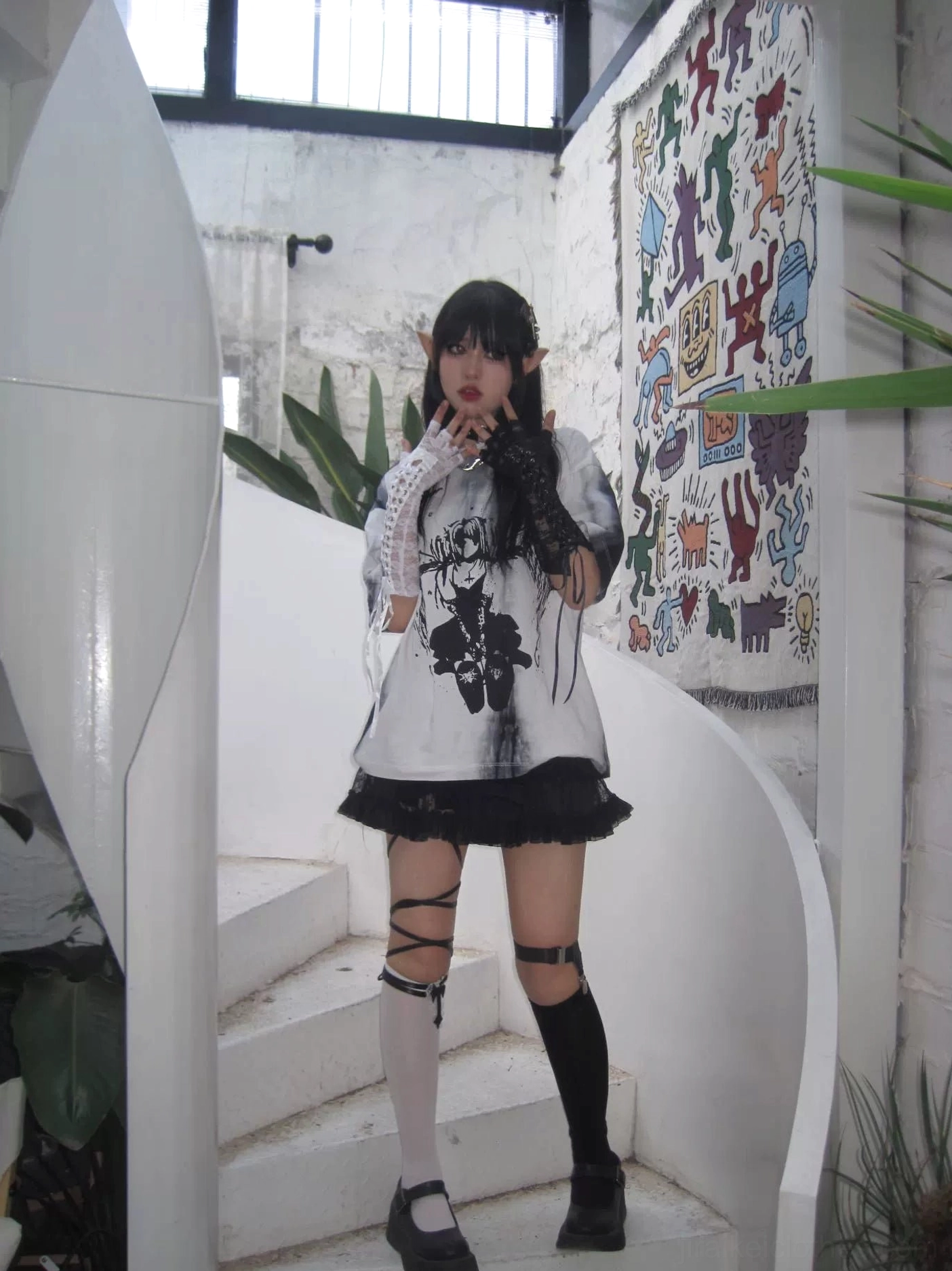 Model with pointed ears wearing celestial angel wings tie-dye gothic jirai kei t-shirt indoors, dark graphic print with ruffled skirt coordination