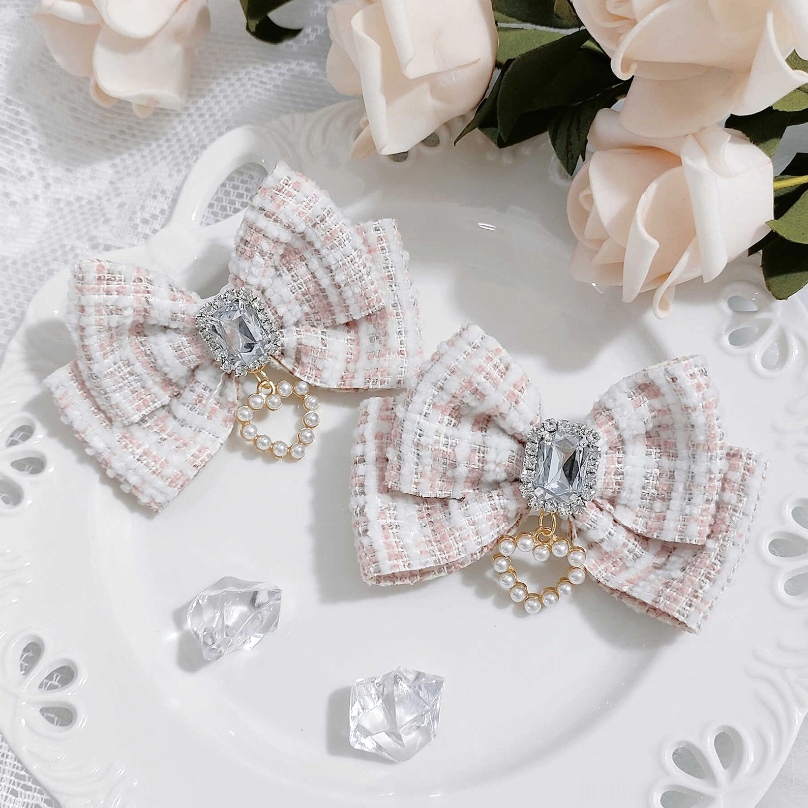 Sweet pink plaid tweed Jirai Kei hair clips with double-bow design, rhinestone embellishments and pearl pendant, styled with roses and crystal decor on white tray, overhead view