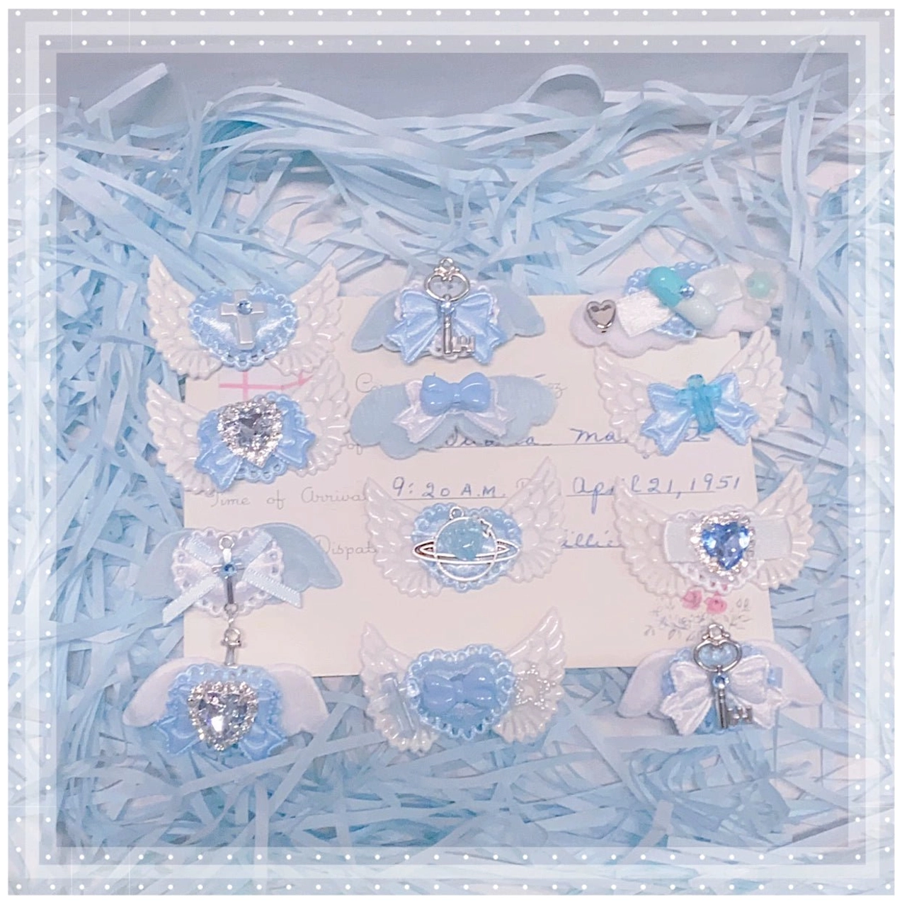 Assorted jirai kei hair clips collection flat lay with blue shredded paper display featuring devil wings heart crosses and rhinestone decorations