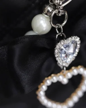 Close-up macro view of Jirai Kei bag charm set with heart crystal pendant and pearl heart ring on black satin background
