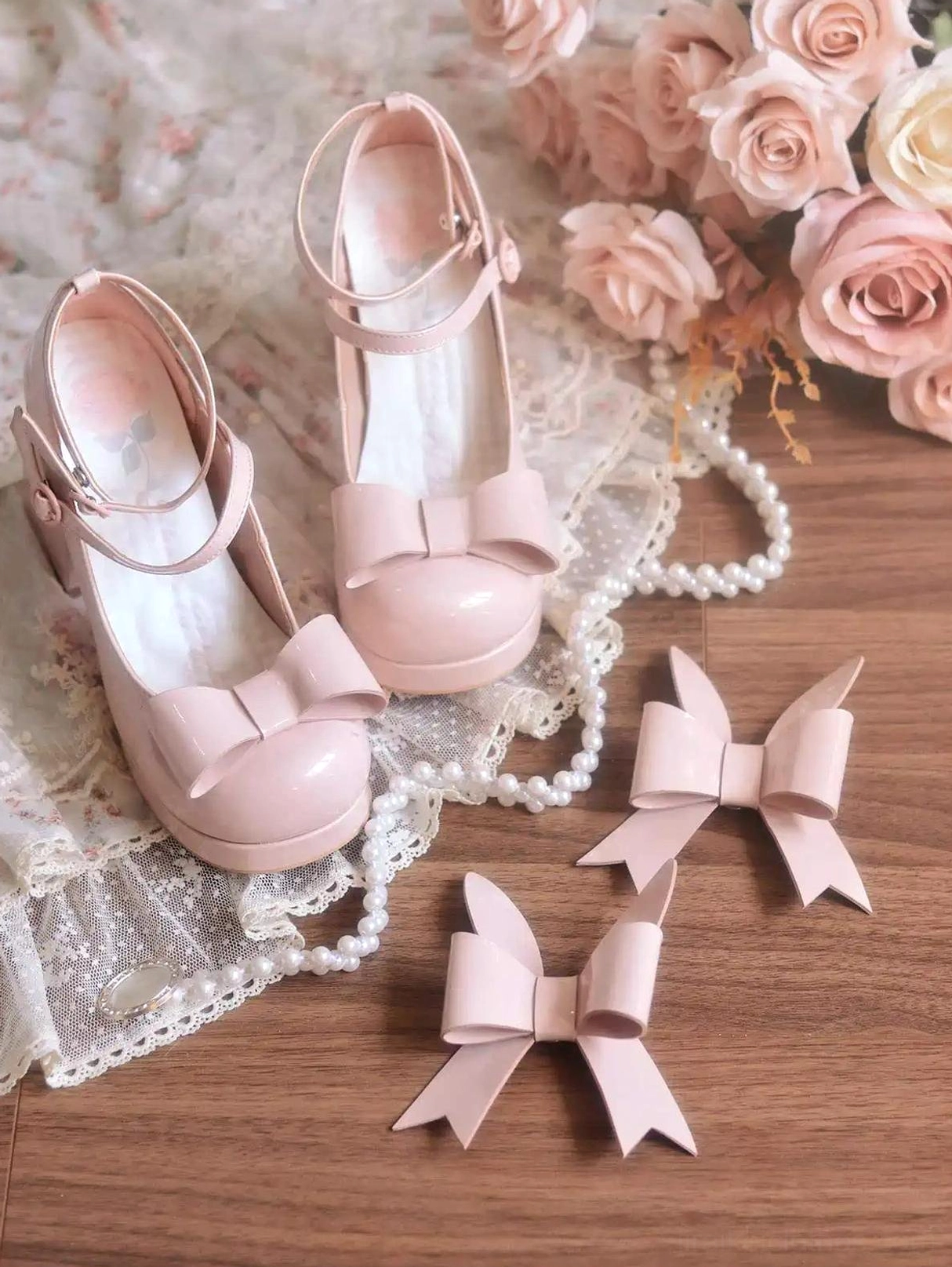 Flat lay top-down view of light pink patent Jirai Kei heels on wooden table with lace decor roses pearls and detachable matching bows