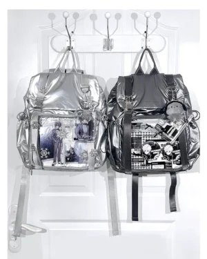 Pair of Jirai Kei ita backpacks in black and silver displayed on white coat hook, featuring decorated badge collages in transparent windows and distinctive star zipper pulls