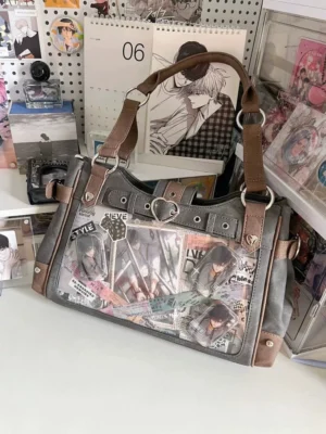 Gun-grey and denim blue two-tone Jirai Kei ita shoulder bag with transparent display panel filled with anime stickers and collectibles, shown on anime-themed desk backdrop