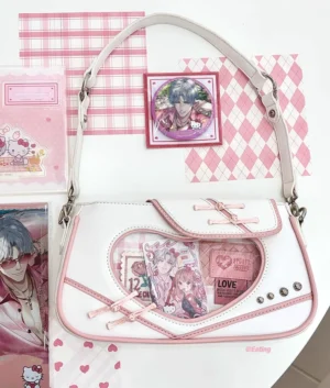 White and pink jirai kei transparent heart itabag crossbody bag with knot button displayed on pink checkered desk with anime merchandise cards and character items