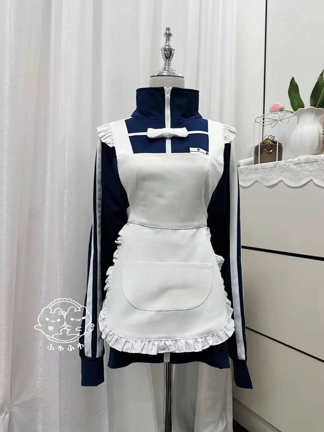 Jirai Kei Jersey Maid combination set displayed on mannequin, showing navy zip-up track jacket with white ruffled apron panel and white maid-style bow decoration, bedroom display setting