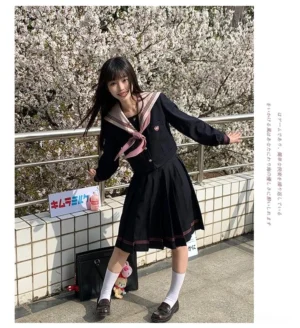Jirai Kei JK uniform three-quarter side angle with model posing arms spread showing the fitted waist construction, navy top with pink trim details, and structured pleated skirt silhouette in outdoor cherry blossom environment