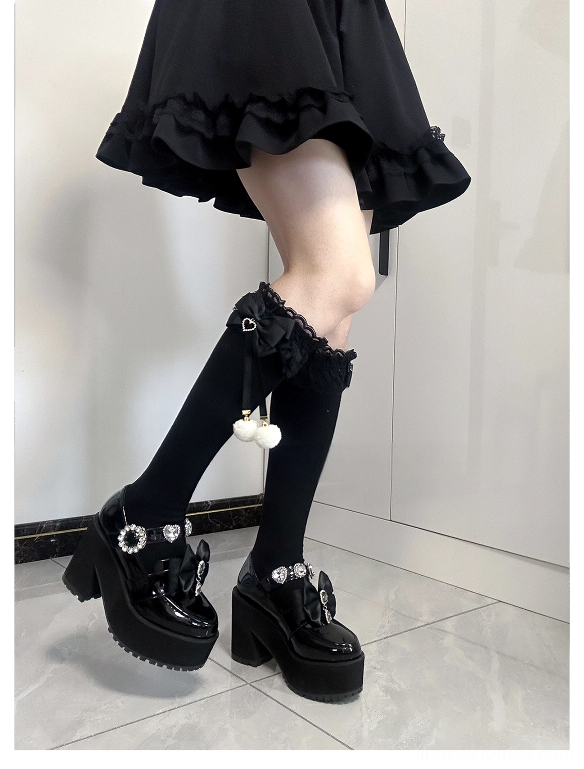 Single styled Jirai Kei knee-high sock low-angle side posed view black knee-length sock lace ruffled cuff hanging white pom-pom accent black ruffled skirt styling