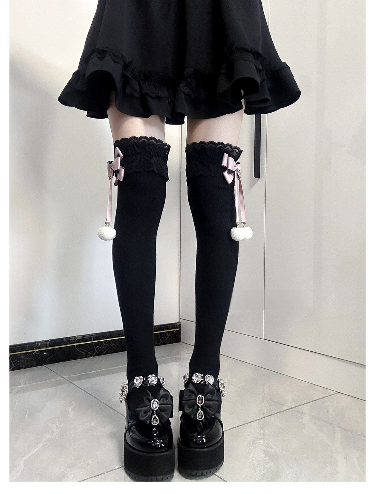 Jirai Kei lace bow pom-pom thigh-high socks front view black fabric with pink bow and white pom-pom detail worn with black ruffled mini skirt and platform leather shoes