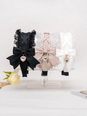 Flat lay front view of multi-color Jirai Kei lace cross bow hairbands with heart diamond charms displayed on acrylic stands with flower props, showing black, white, and ashy-pink color options