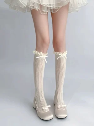 Beige lace mid-calf Jirai Kei scrunchy socks with ruffled satin bow cuff, front full low-angle view on model wearing ballet flats and tulle skirt