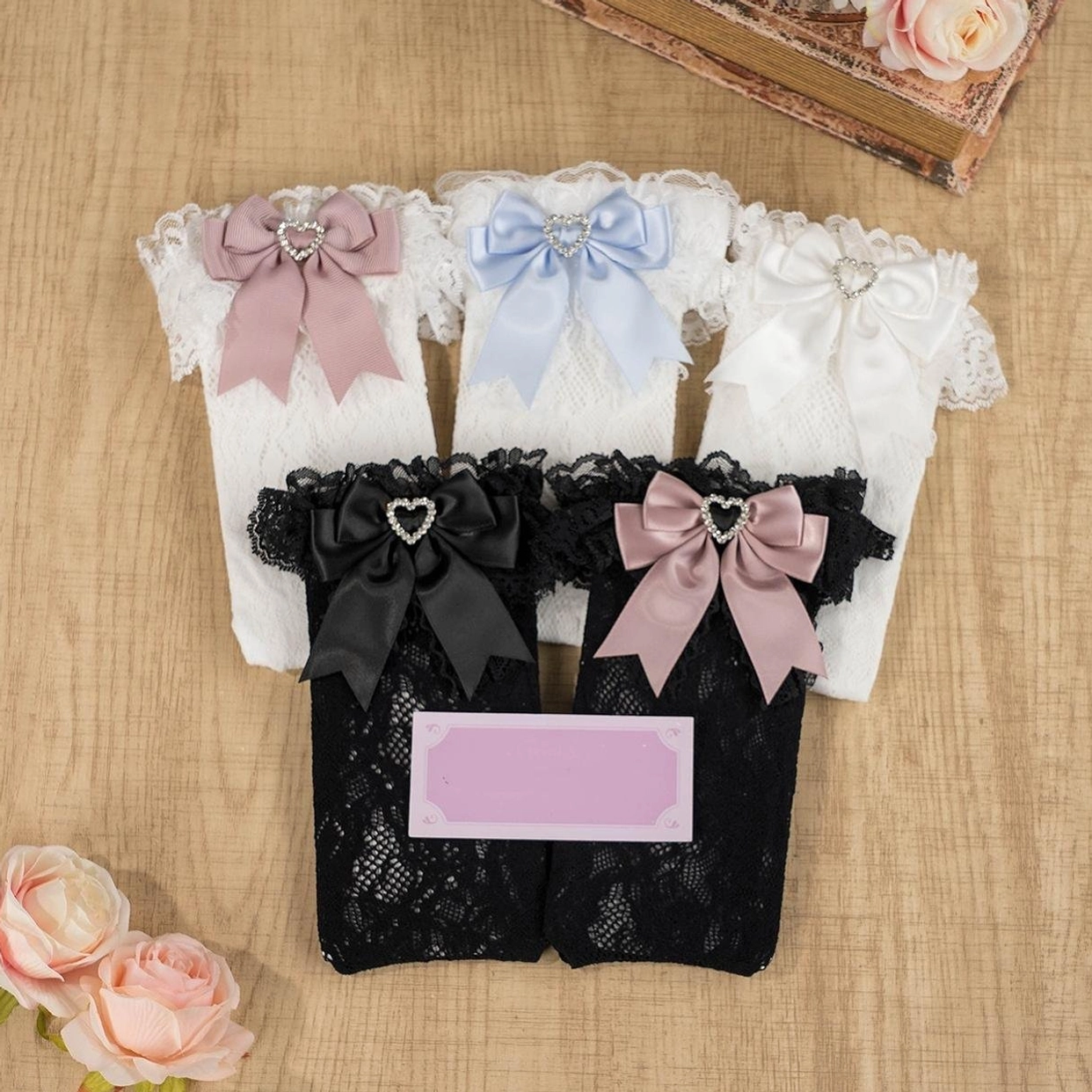 Flat lay display of multi-color jirai kei lace socks with assorted satin bows and heart rhinestone accents arranged with roses on wooden table