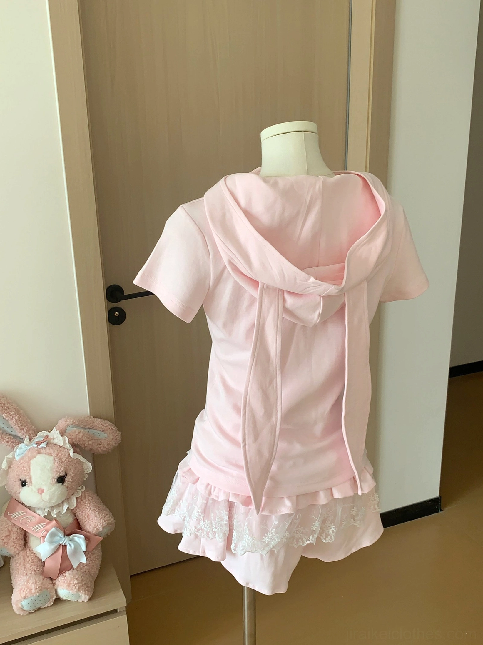 Light pink zip-up short-sleeve crop top without hood and lace ruffle mini skirt laid flat with adorable plush toy accessory
