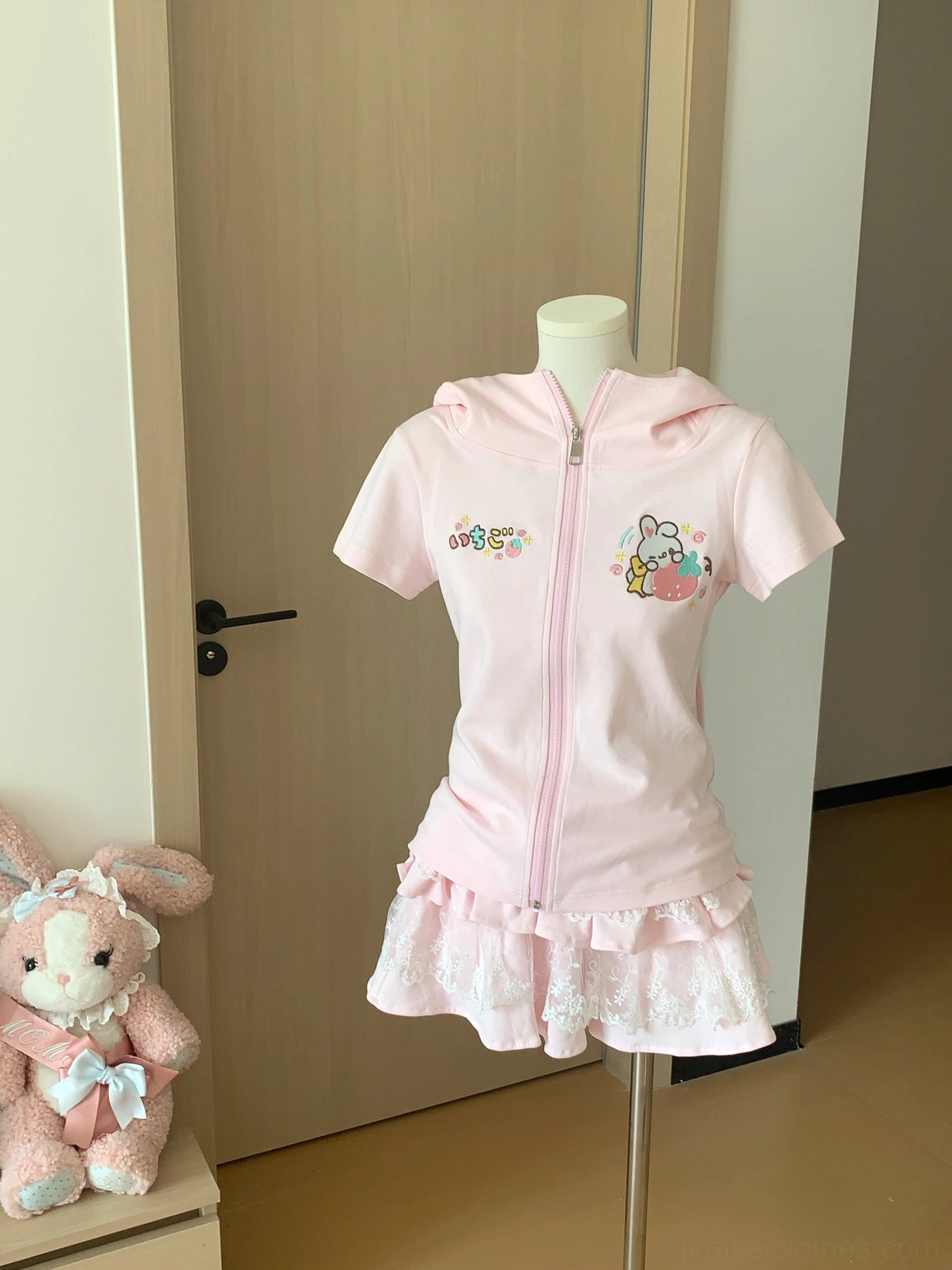 Light pink zip-up hoodie with cartoon prints and single-layer lace ruffle mini skirt displayed flat with cute plush rabbit toy