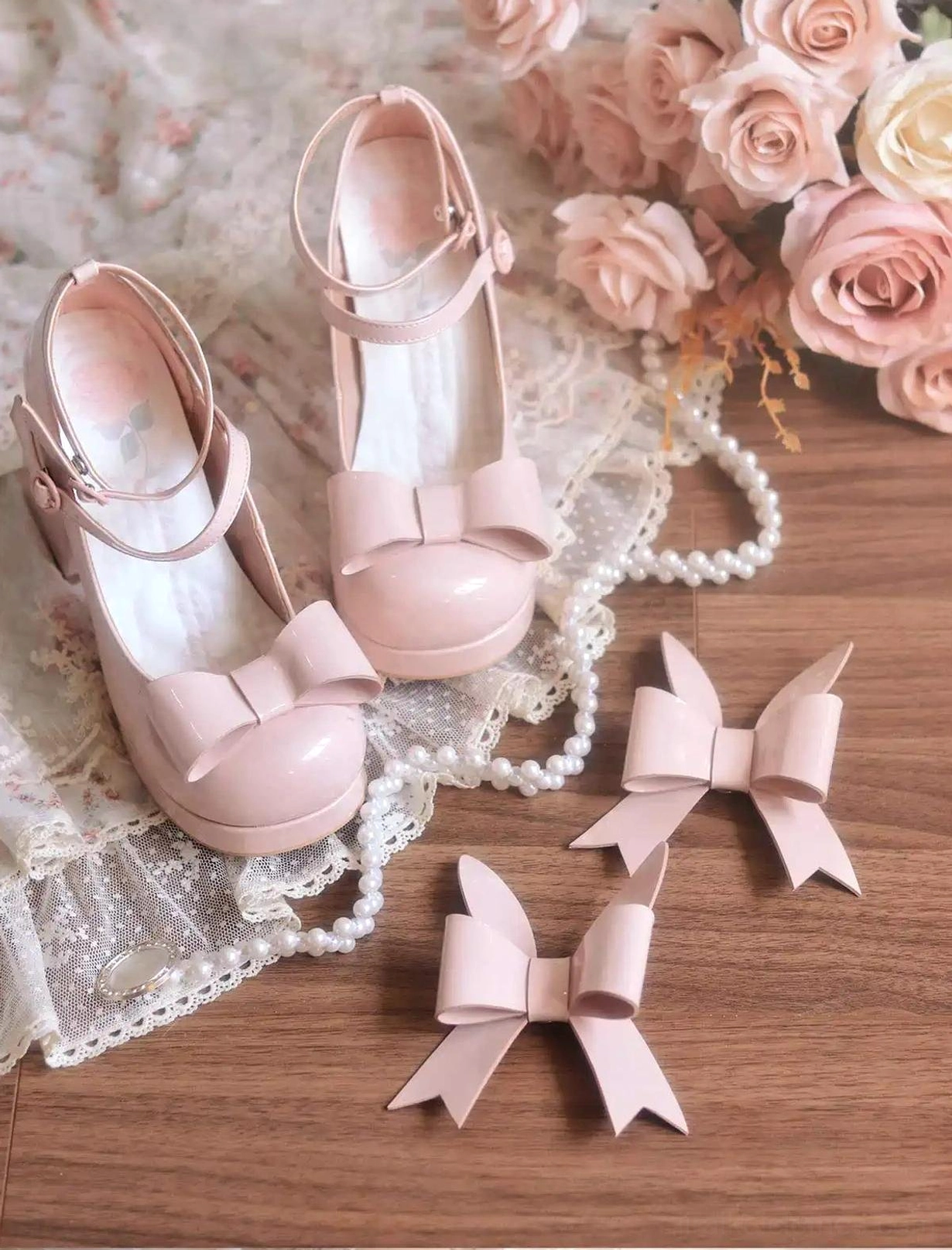 Overhead flat lay of light pink patent Jirai Kei Mary Jane heels with ankle strap front bow round toe and extra decorative bows on vintage wooden surface