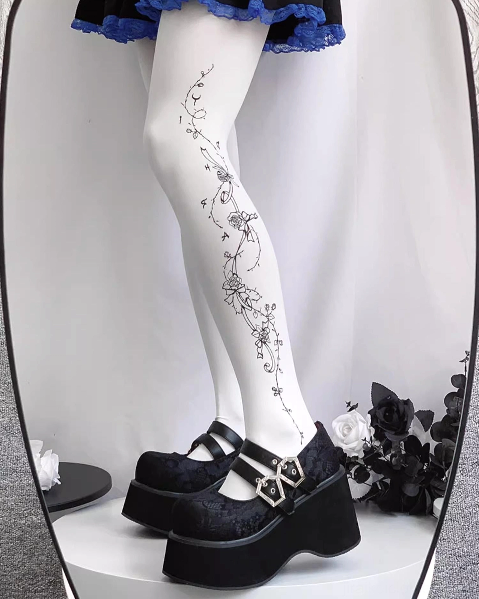 Mary Jane platform shoes on model legs wearing floral tattoo tights with black velvet upper dual silver buckles thick platform sole and blue frill skirt hem