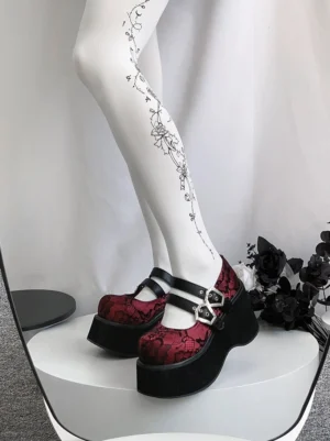 Gothic platform Mary Jane shoes with red patterned lace upper and dual silver hexagonal buckles displayed on white stand with gothic floral decoration