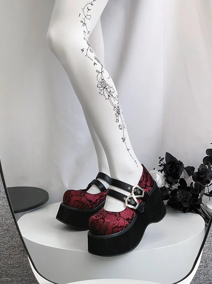 Gothic platform Mary Jane shoes with red patterned lace upper and dual silver hexagonal buckles displayed on white stand with gothic floral decoration