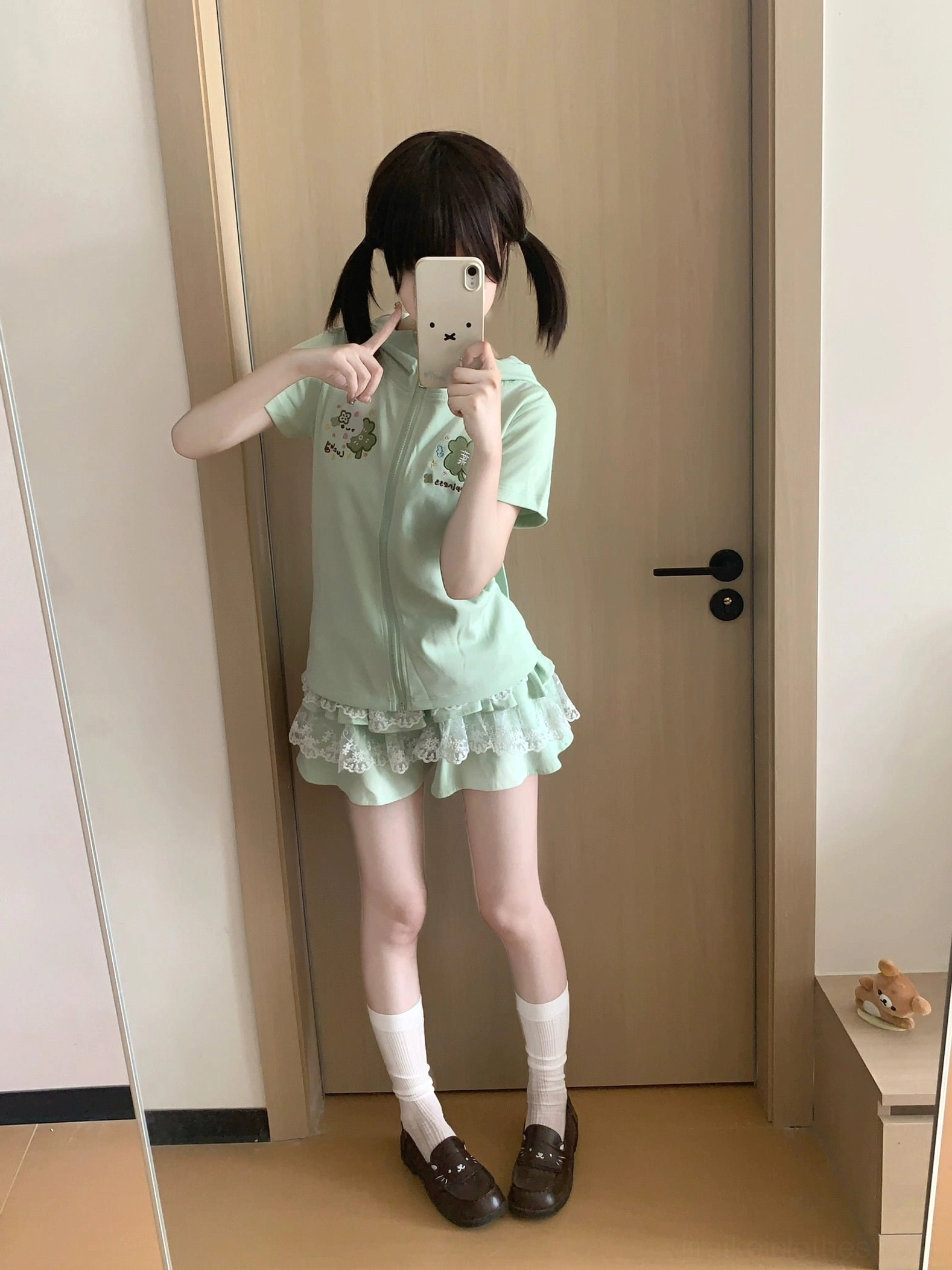 Mint green Jirai Kei kawaii loungewear on model making heart hand gesture, showing short-sleeve zip hoodie with bunny ear hood and embroidered details with lace skirt