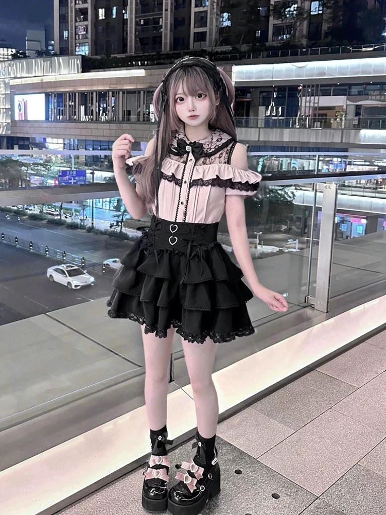 Front full-body view of Jirai Kei two-piece set with bow neckline, button-front blouse design, and black layered ruffled skirt with heart waist decorations worn at outdoor night venue