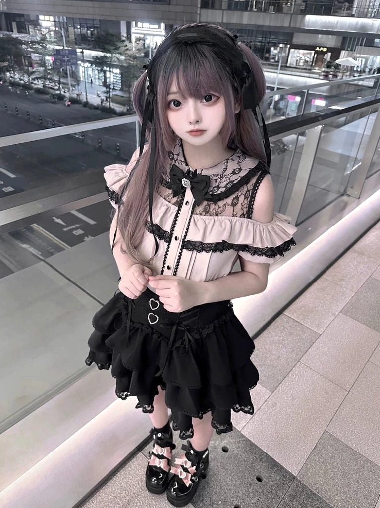 Medium-distance front view of Jirai Kei off-shoulder two-piece outfit with bow neck decoration, ruffled sleeves, and black tiered skirt worn at outdoor night shopping district