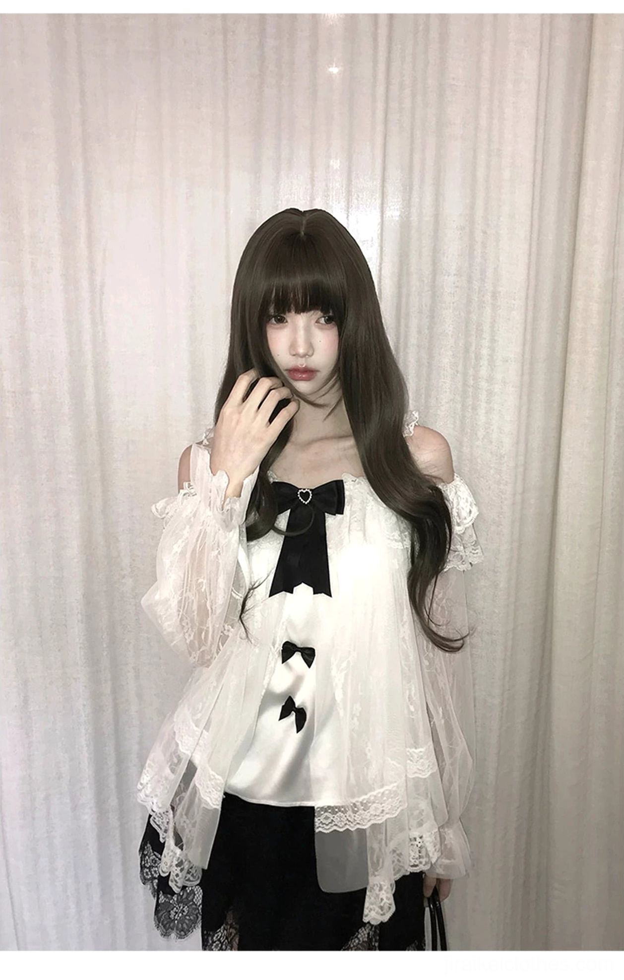 Half-body front close-up of off-shoulder blouse worn by model with long wavy brown hair, showing delicate ruffled neckline, black bow decorations, and sheer tulle fabric texture
