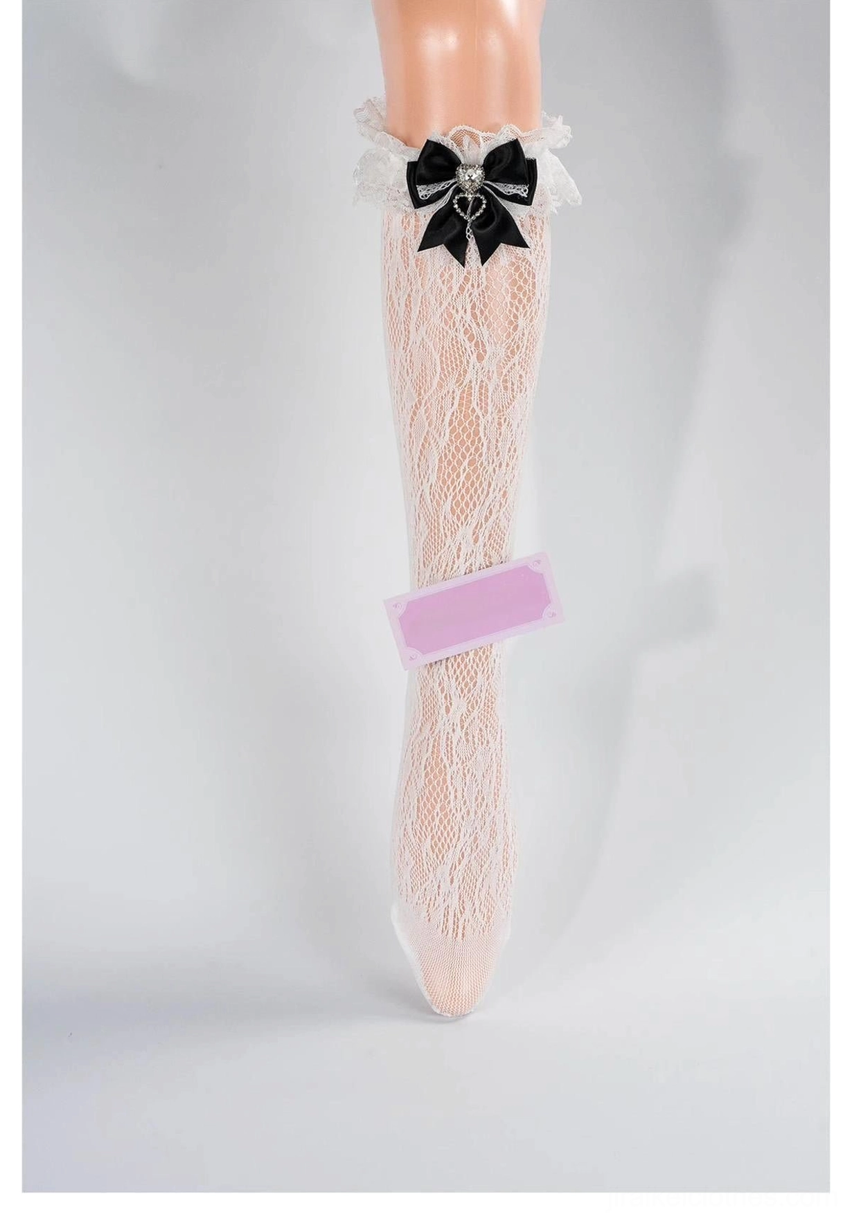 Off-white lace mid-calf Jirai Kei socks with ruffled lace cuff, black bow and heart rhinestone accent, front full view on mannequin