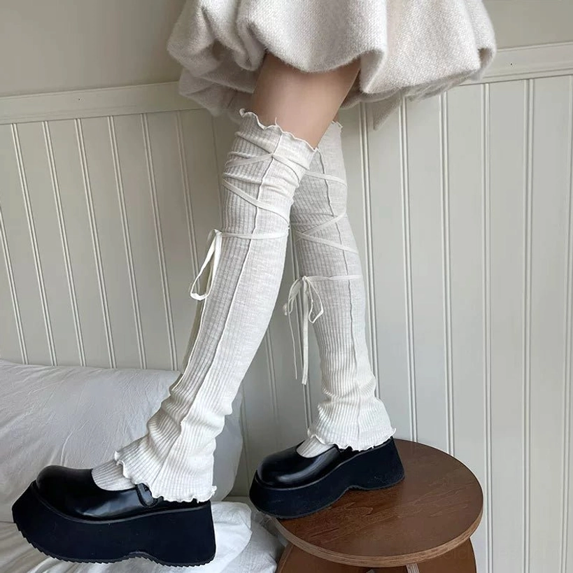 Off-white ribbed knitted over-the-knee leg warmers with side crisscross lace-up ties slouchy fit side profile view model wearing black platform loafers indoor setting