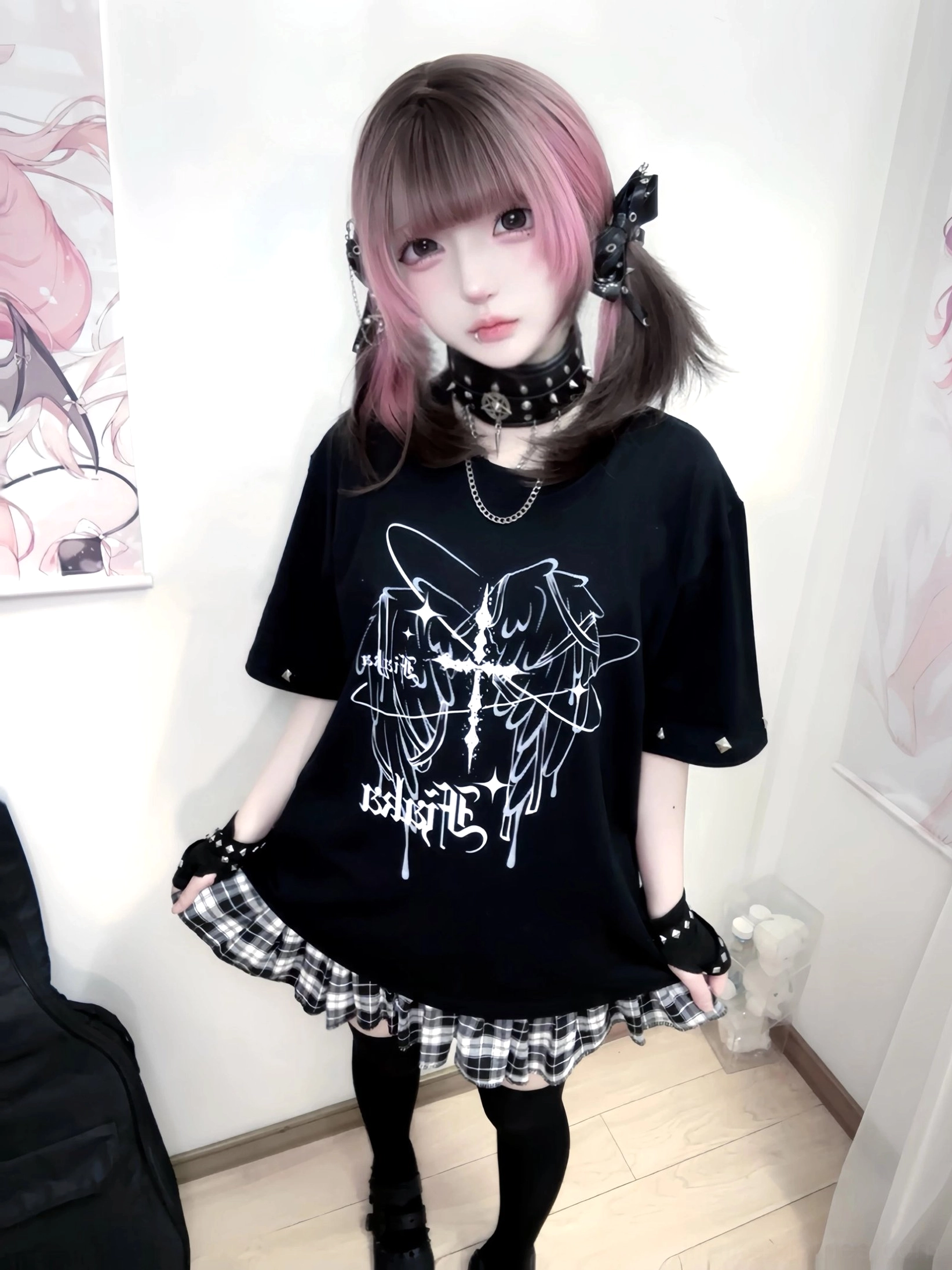 Black oversized Jirai Kei graphic t-shirt with white gothic wing-cross print and studded cuffs, front full-body shot on female punk model wearing plaid skirt and thigh-high socks in bedroom setting
