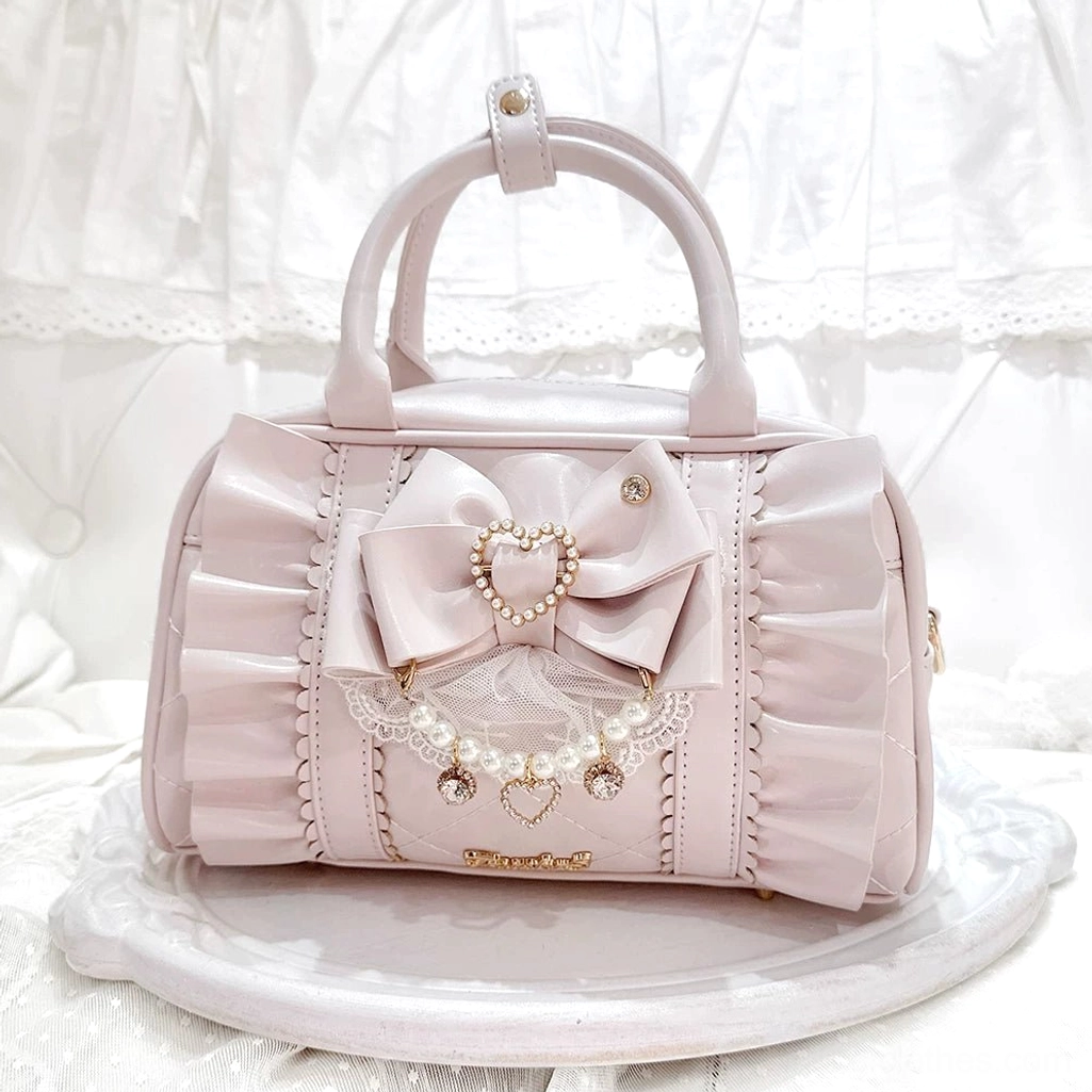 Pastel pink Jirai Kei 2-way handbag with ruched leather and detachable bow-pearl charm, front flat lay view on white lace backdrop