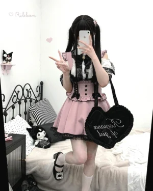 Pink and black Jirai Kei lace cold-shoulder blouse with bow tie, petal-shaped lace collar detail, full front view on model in bedroom setting