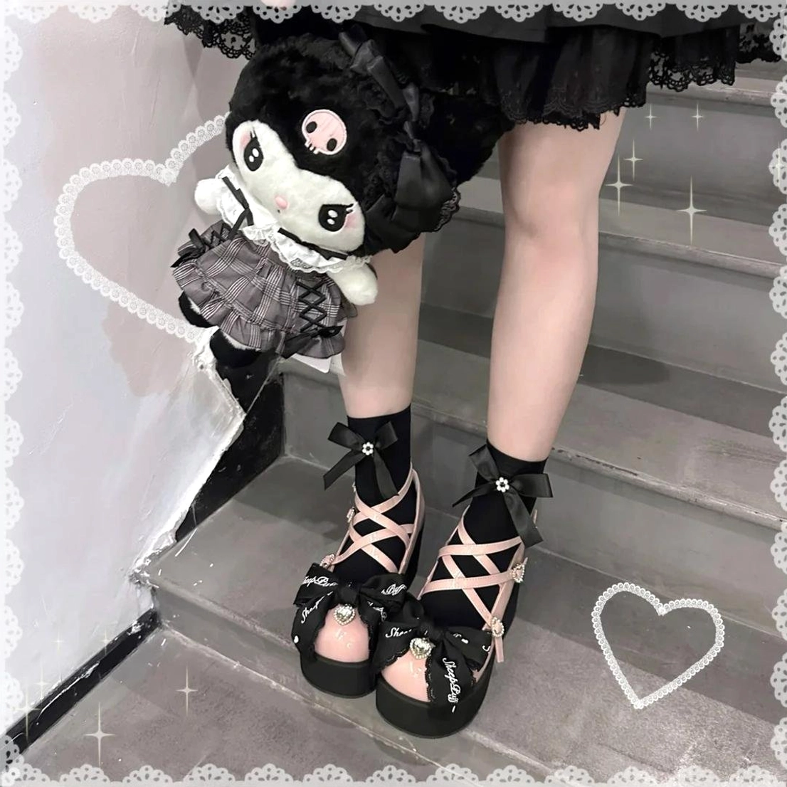 Back view of pink and black platform Mary Jane shoes on model wearing black socks, stairs scene with Kuromi plush toy, ankle buckle straps and bow ornaments visible