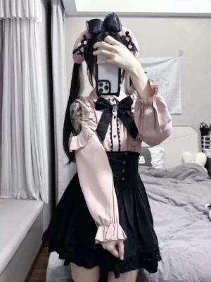 Jirai Kei style model wearing pink blouse with asymmetrical lace cutout shoulders and black corset waistband skirt, demonstrating waist-cinching silhouette and delicate lace details of the complete set