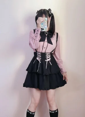 Full-body Jirai Kei two-piece outfit with dusty pink Peter Pan collar blouse and black lace-up suspender skirt with tiered ruffles, twin-tailed model mirror selfie in plain room