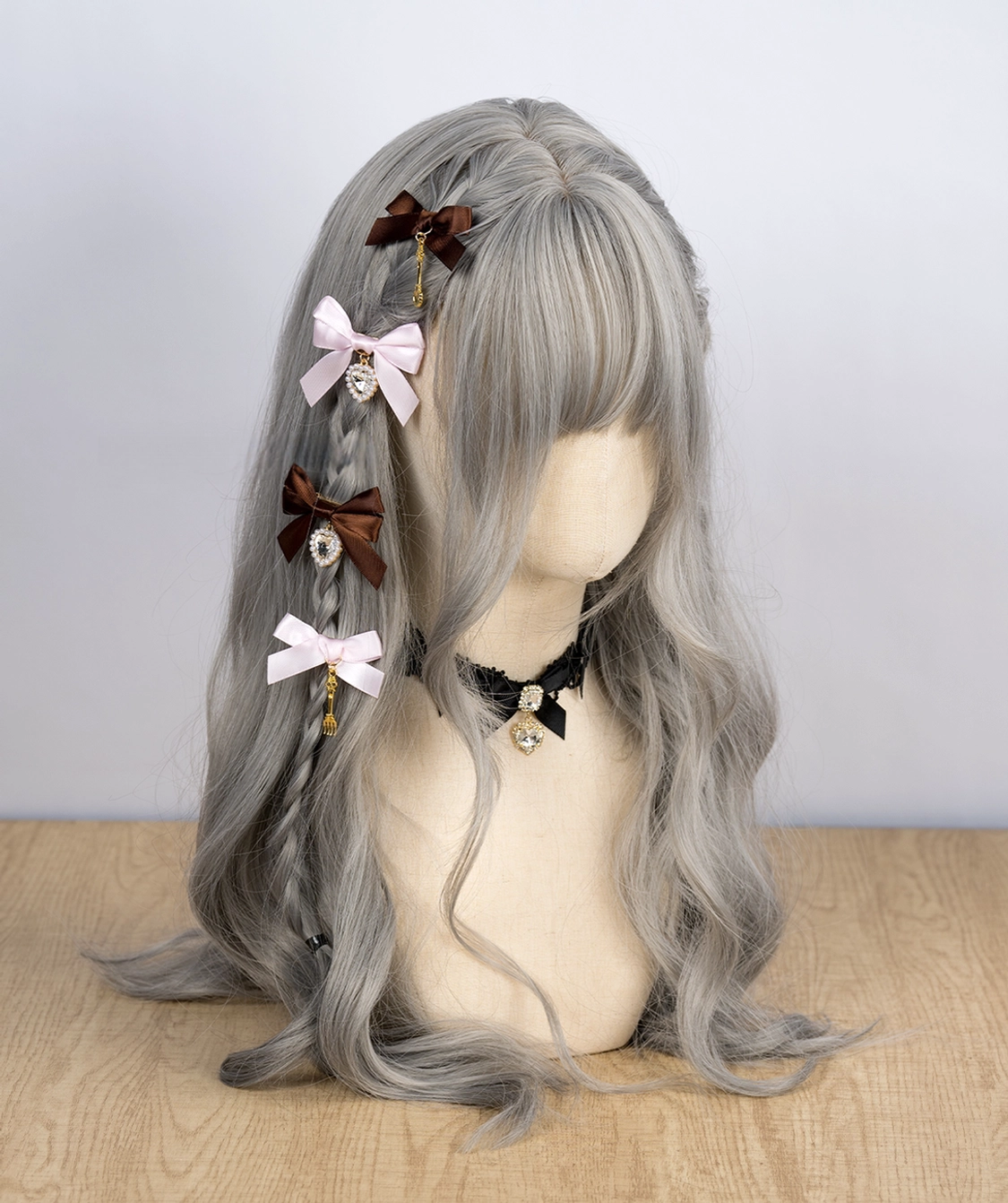 Light pink and dark brown Jirai Kei bow hair clips with rhinestone and bell pendant charms on mannequin with gray wig and vintage lace choker