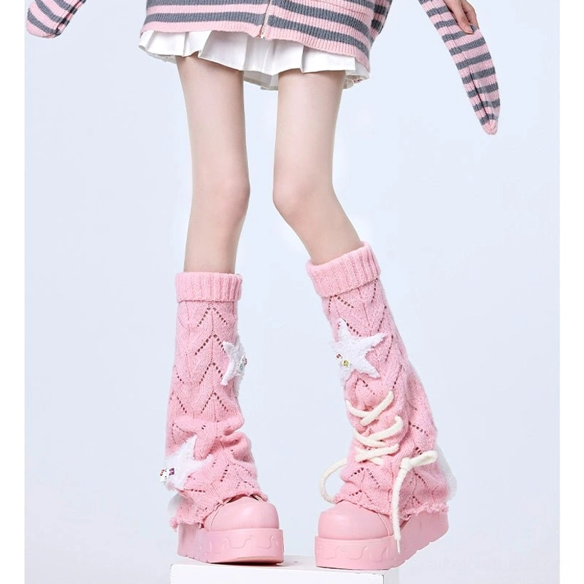 Front lower body shot of blush pink Jirai Kei leg warmers with hollow knit texture and star accents, worn with cropped striped top against white studio background, showing lace-up front design detail