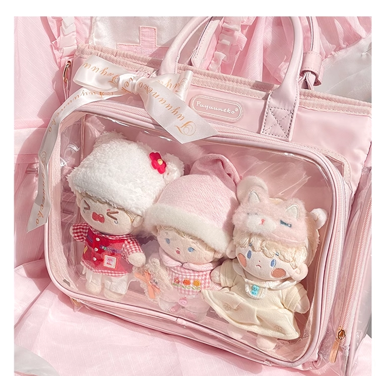Front flat close-up of pink Jirai Kei itabag with transparent window displaying three 20cm plush dolls, satin ribbon accent on top handle