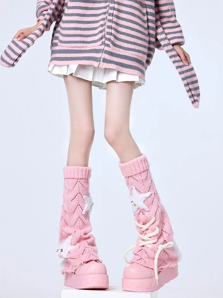 Blush pink Jirai Kei knit leg warmers with lace-up front straps and star patch decorations, paired with grey-pink striped cardigan in studio setting, displaying thick knitted fabric quality