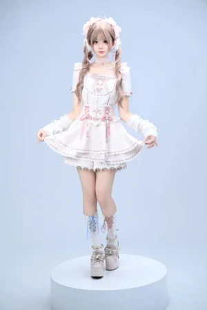 Full-body front view of pink maid-style Jirai Kei lolita outfit with ruffled lace trim and puff short sleeves on studio blue backdrop