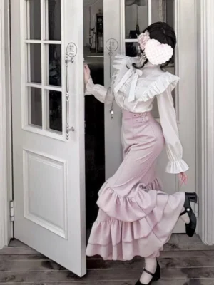 Three-quarter side view of Jirai Kei pink mermaid skirt and white blouse ensemble with dramatic bell sleeves and adjustable buckle straps on model wearing black heeled shoes