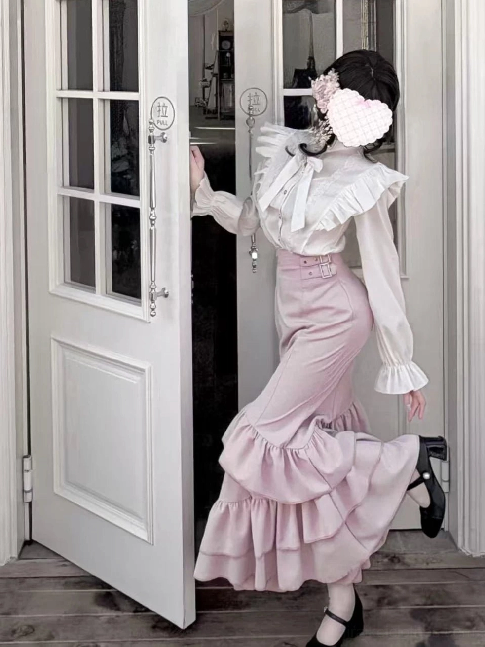 Three-quarter side view of Jirai Kei pink mermaid skirt and white blouse ensemble with dramatic bell sleeves and adjustable buckle straps on model wearing black heeled shoes
