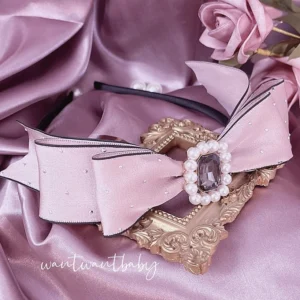 Pink pearl rhinestone double-bow Jirai Kei headband flat lay with fake roses on pink satin fabric, showing intricate gem and pearl details