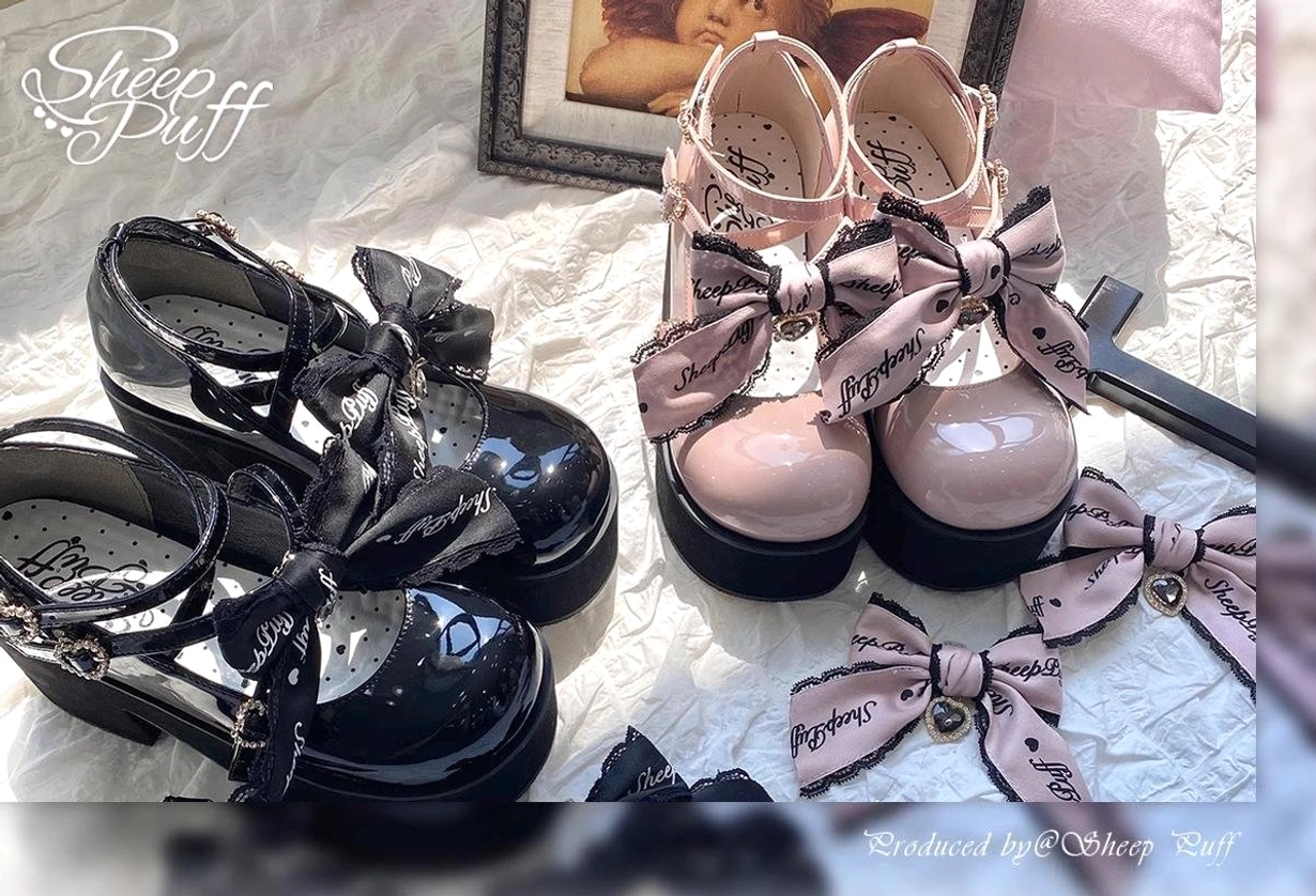 Pink platform Mary Jane Jirai Kei shoes with black platform sole, crisscross buckle straps, heart-shaped decorative hardware, and interchangeable bow ornaments