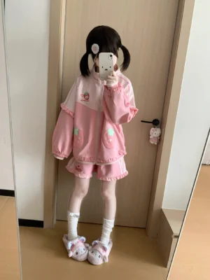 Jirai Kei pink strawberry embroidered two-piece set worn by model with twin-tailed hairstyle in full-body mirror selfie, showcasing loose-fit coat with ruffled trim and matching strawberry shorts with bow embroidery