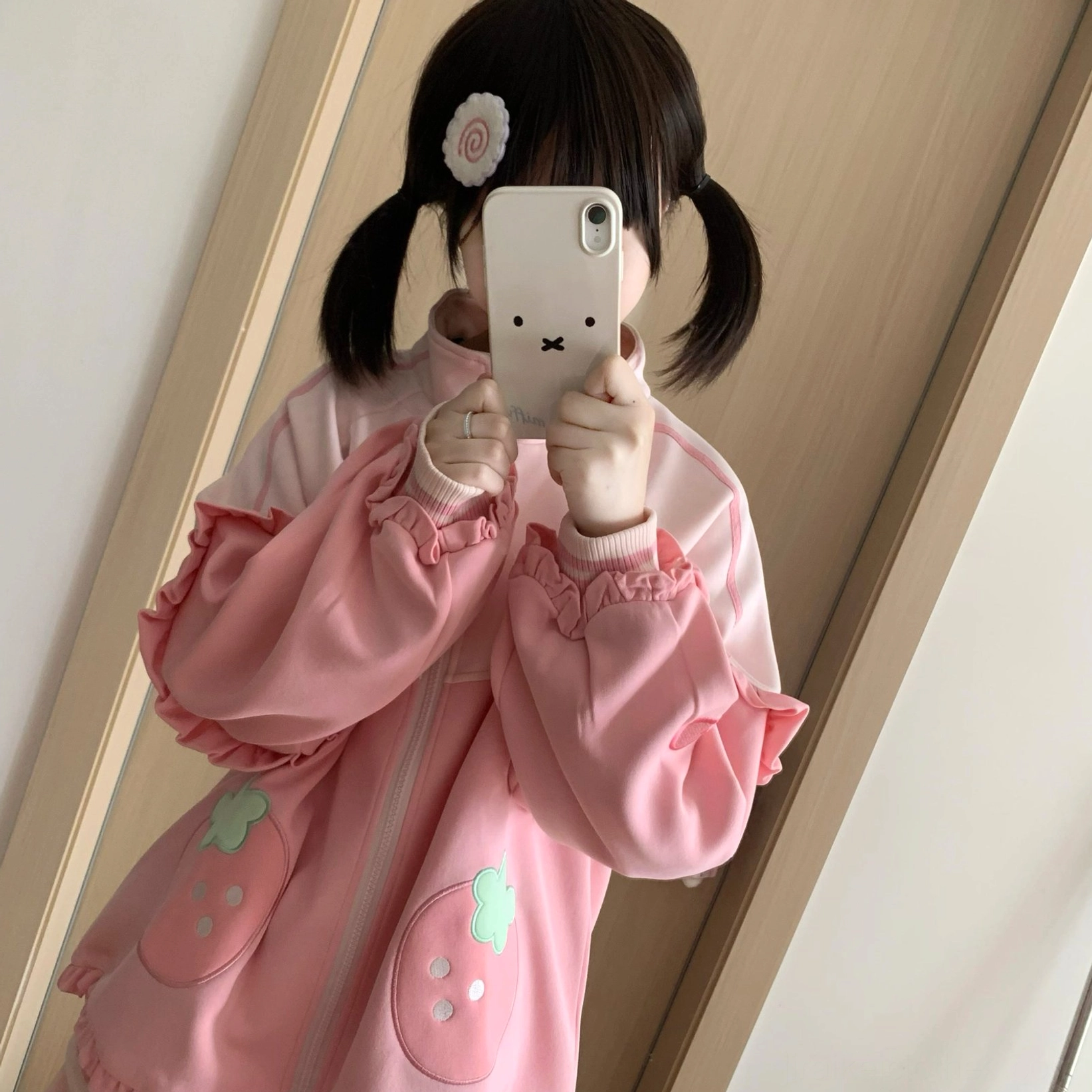 Front mirror selfie view of pink strawberry Jirai Kei two-piece set on model holding smartphone, demonstrating oversized coat style with strawberry embroidery and comfortable shorts fit
