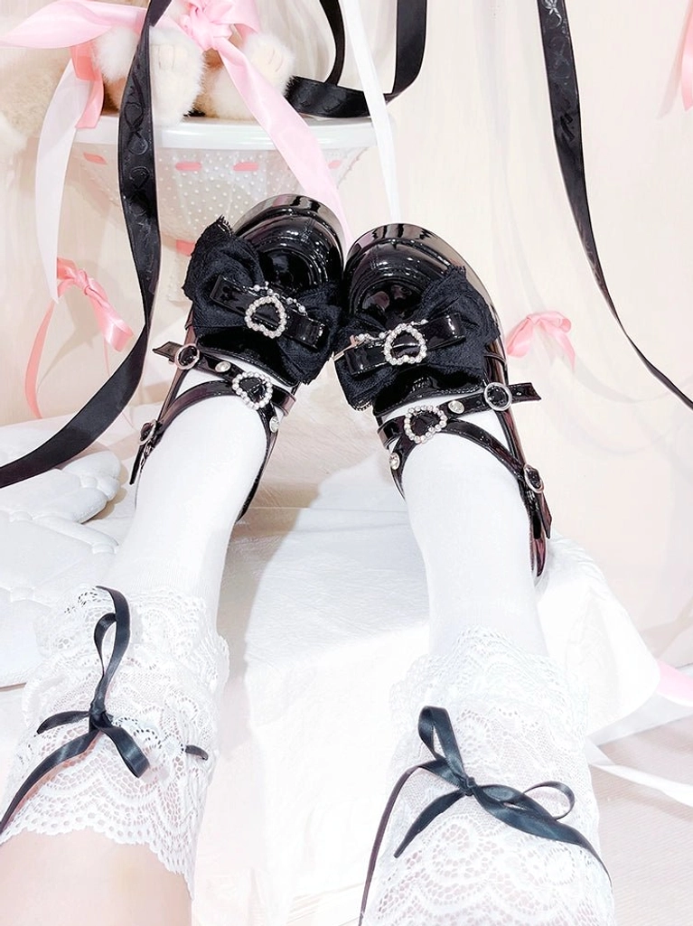 Top-down flat lay view of black Jirai Kei high-heel platform shoes showing heart-shaped rhinestone buckles, ankle bow straps, and smooth patent leather upper surface
