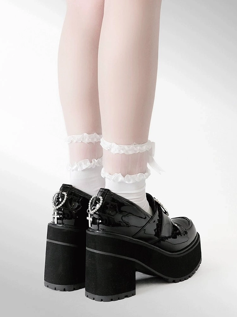 Back close-up view of black glossy patent leather platform loafers showing back zipper detail on heel, chunky block heel construction, and frilled ruffle white ankle socks