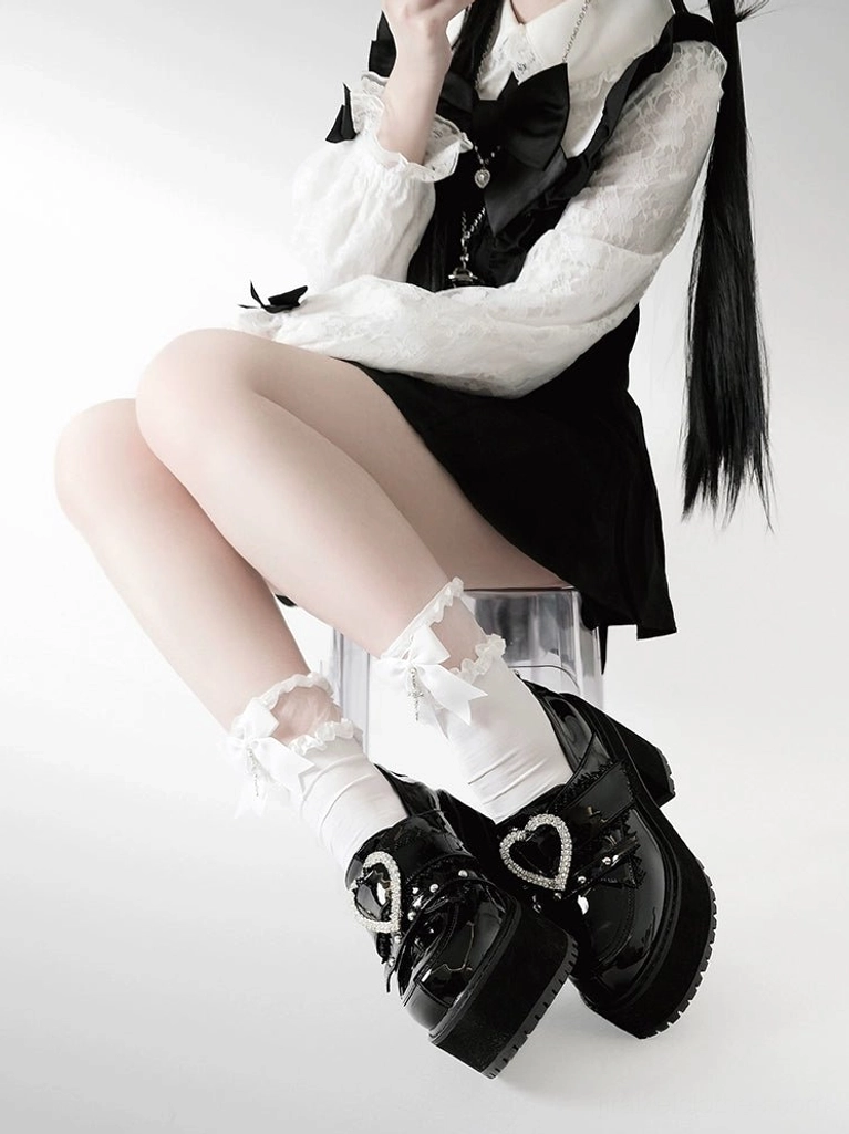 Seated side view of model in jirai kei outfit sitting on clear stool wearing black patent leather heart buckle platform loafers with matching frilled socks, showcasing full outfit coordination